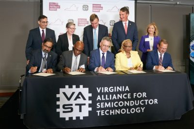People sitting at a table on a stage signing papers.